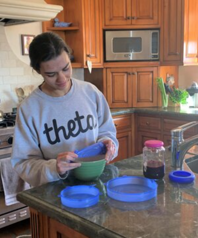 A girl wraps a bowl of food with a reusable silicone lid.